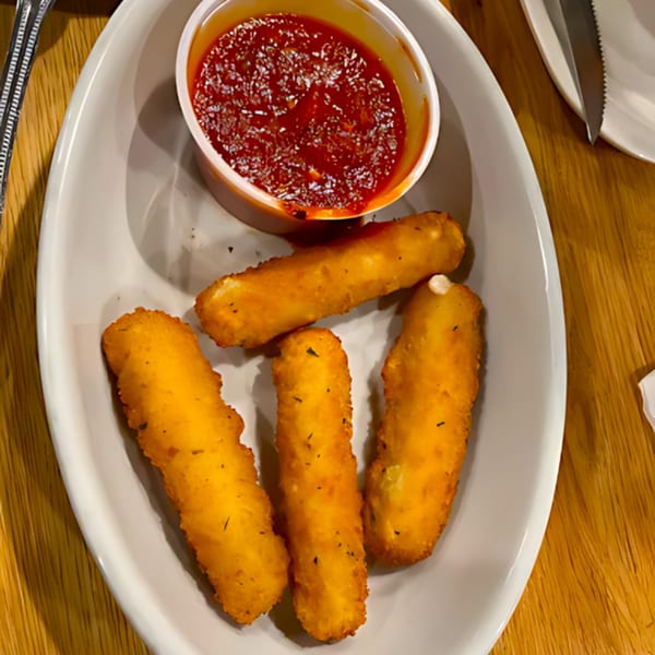 Four golden-brown mozzarella sticks with a side of red marinara sauce on a white plate.