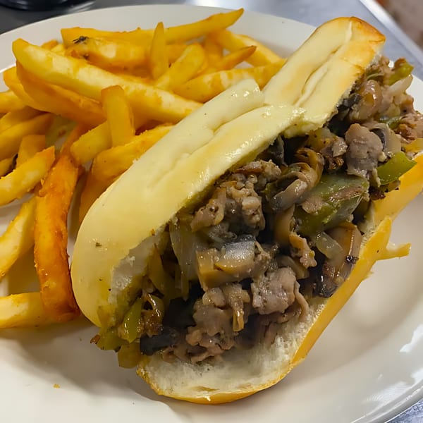 A cheesesteak sandwich with mushrooms, onions, and peppers, served with a side of golden french fries.