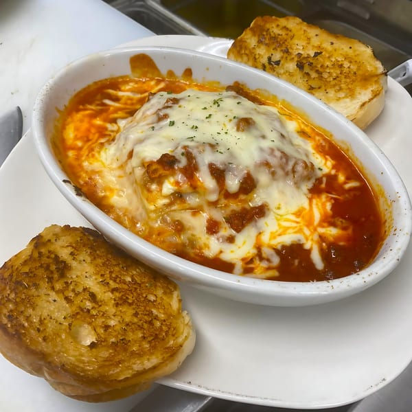 Baked ziti with melted cheese and marinara sauce, served with two slices of garlic bread.