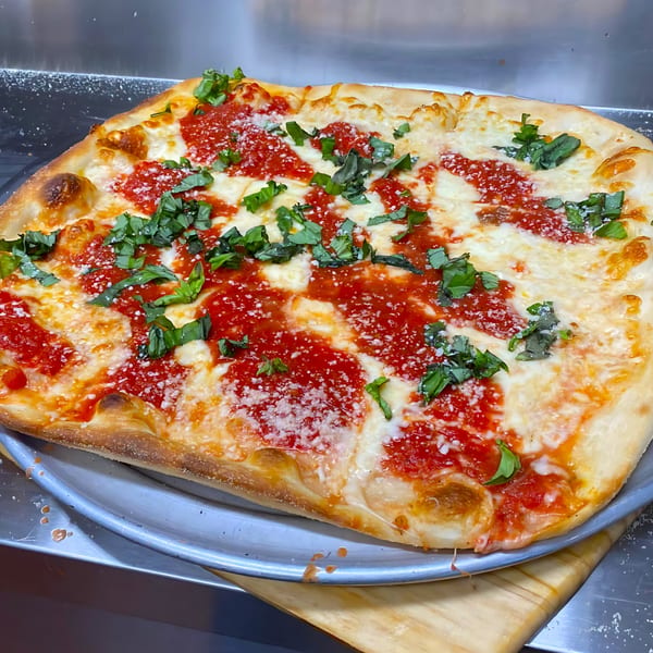 A rectangular Sals pizza with red sauce, melted mozzarella, fresh basil, and grated cheese.