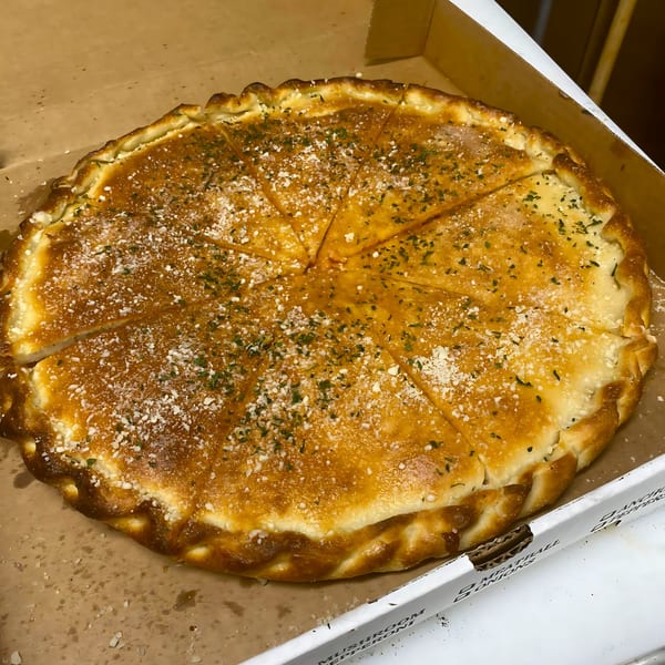 A golden-brown, round calzone from Sal's Pizza, sliced into wedges, sprinkled with parmesan and herbs.