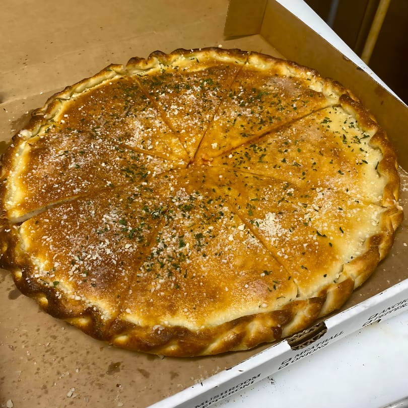 A golden-brown, round calzone from Sal's Pizza, sliced into wedges, sprinkled with parmesan and herbs.